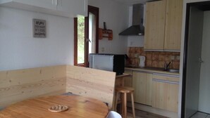 Kompakti keittiö, jossa on puiset kaapit, sisäänrakennettu liesi ja pieni ruokailutila, jossa on puinen pöytä ja valkoiset tuolit.