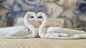 Two towels arranged in the shape of a heart on a textured bed. - Jardins de São Luís (Setubal)