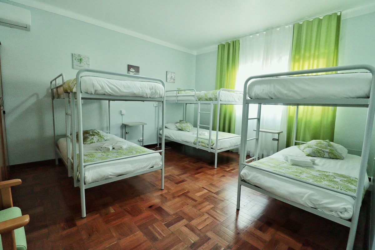 Un dormitorio con literas, suelo de madera y una ventana con cortinas verdes.