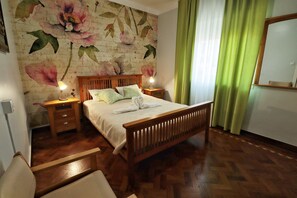 A neatly made bed with a wooden headboard, two bedside tables with lamps, and a floral wallpaper. - Jardins de São Luís (Setubal)