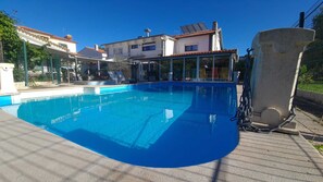 A swimming pool with a clear blue water, surrounded by a fence, and adjacent to a building with a tiled roof. - Jardins de São Luís (Setubal)