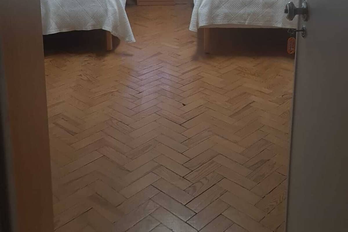 Pequeña habitación individual con dos camas, una ventana con cortinas, una mesita de noche y una lámpara en el techo.