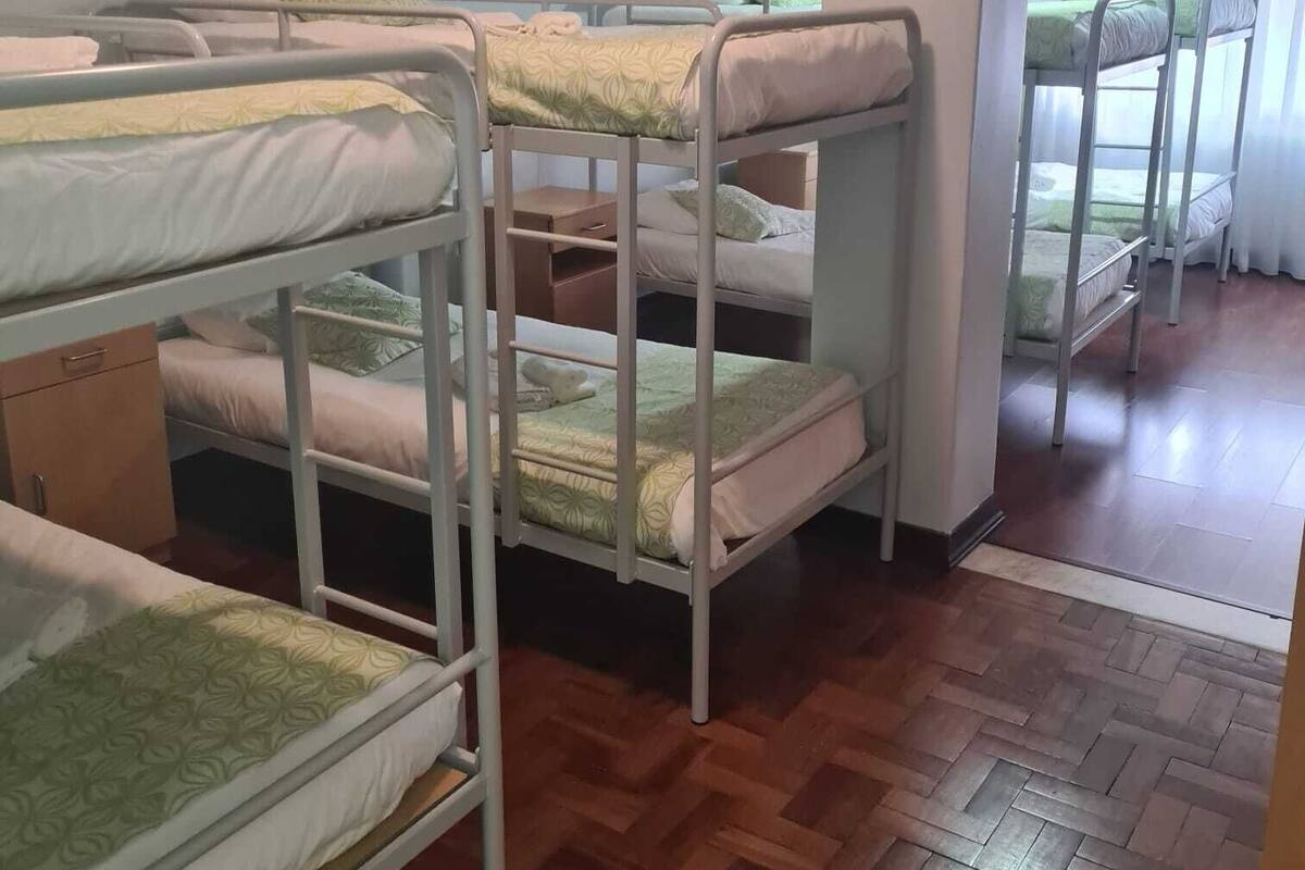 Una habitación con literas, suelo de madera y una ventana con cortinas.