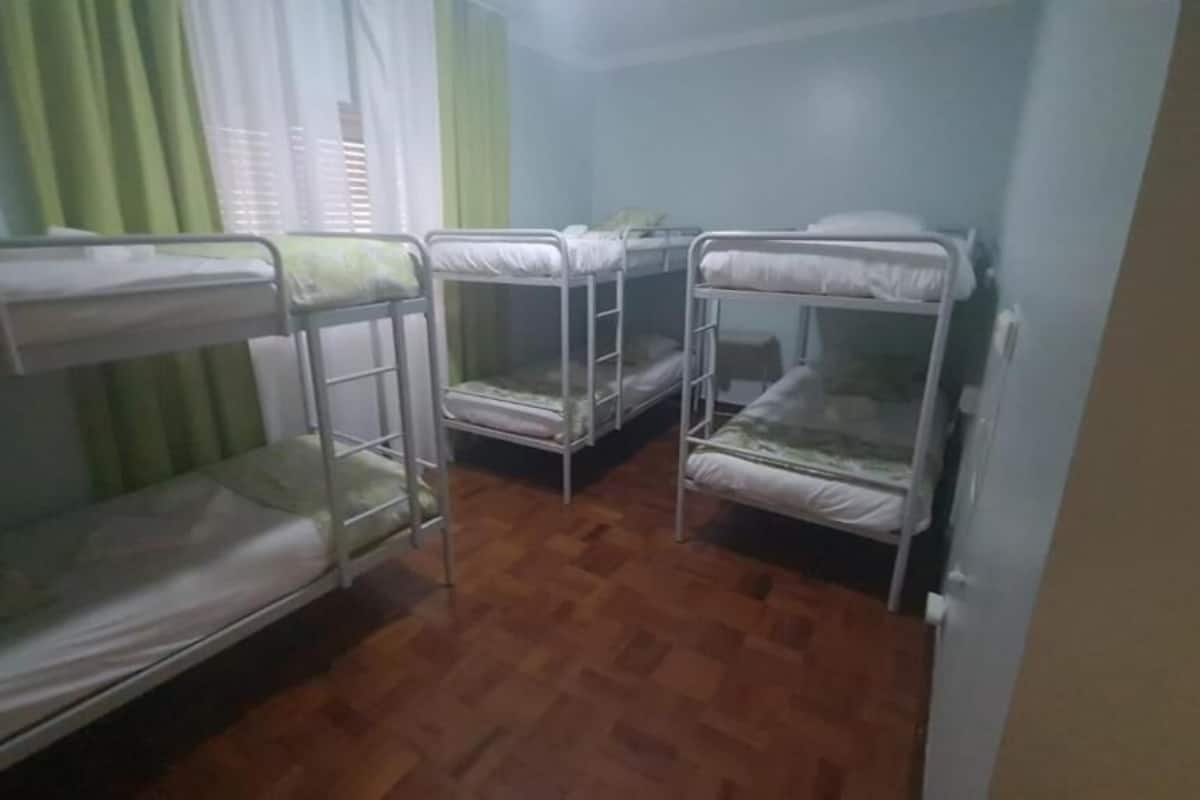 Una habitación con tres literas, suelo de madera y una ventana con cortinas.