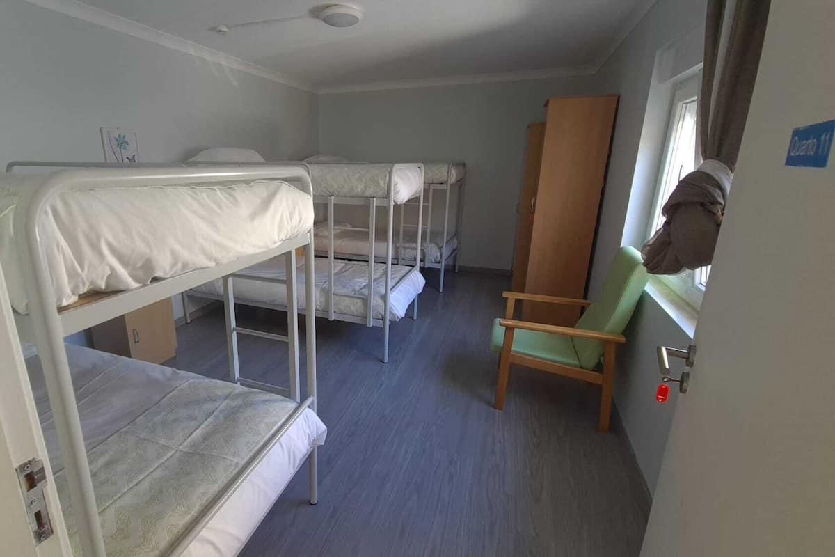 Una habitación con literas, una silla de madera y una ventana.