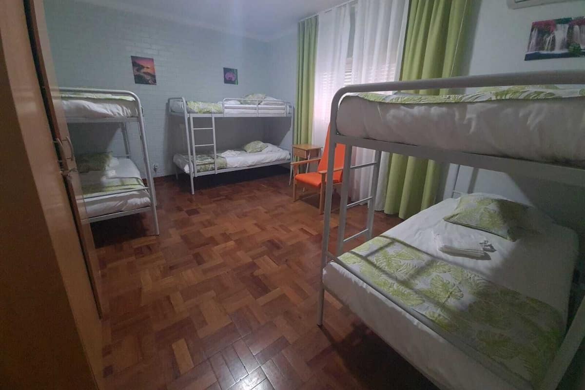 Un dormitorio con literas, suelo de parqué de madera y una ventana con cortinas.
