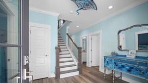 A hallway with a wooden staircase, a blue vanity with a mirror, and a door leading to another room. - Brand New, Golf Cart Included - 546 Remora Dr. (Fripp Island)