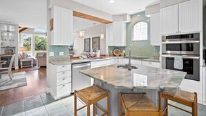 A modern kitchen with white cabinetry, a large island with bar stools, and built-in appliances. - Lakefront, Golf Cart Included, Pet Friendly - 259 Deer Run (Fripp Island)