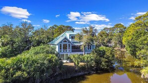 A house with a green roof, surrounded by dense greenery and a body of water. - Lakefront, Golf Cart Included, Pet Friendly - 259 Deer Run (Fripp Island)