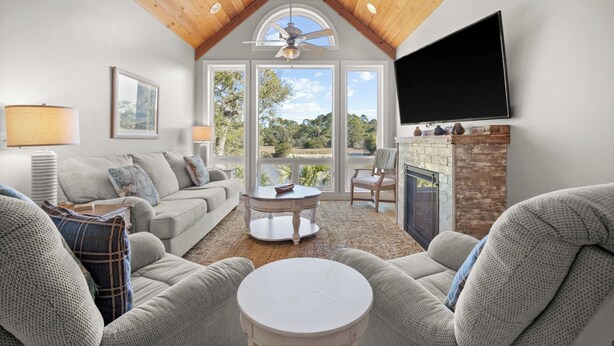 A spacious living room with a high ceiling, a fireplace, a television, and a large window offering a view of the outdoors. - Lakefront, Golf Cart Included, Pet Friendly - 259 Deer Run (Fripp Island)