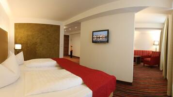 Ein Hotelzimmer mit einem großen Bett, einer roten Tagesdecke, einem Flachbildfernseher an der Wand und einem rot gestreiften Sofa in der Ecke.