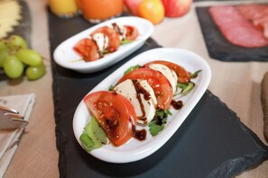 Two white plates with a salad of tomatoes, mozzarella, and greens on a black slate board. - Altstadt-Hotel Passau (Passau)