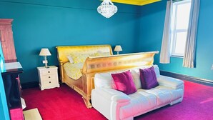 A bedroom with a bed, a white sofa, a nightstand, a lamp, and a chandelier. - PHOENIX Apartments (Goole)