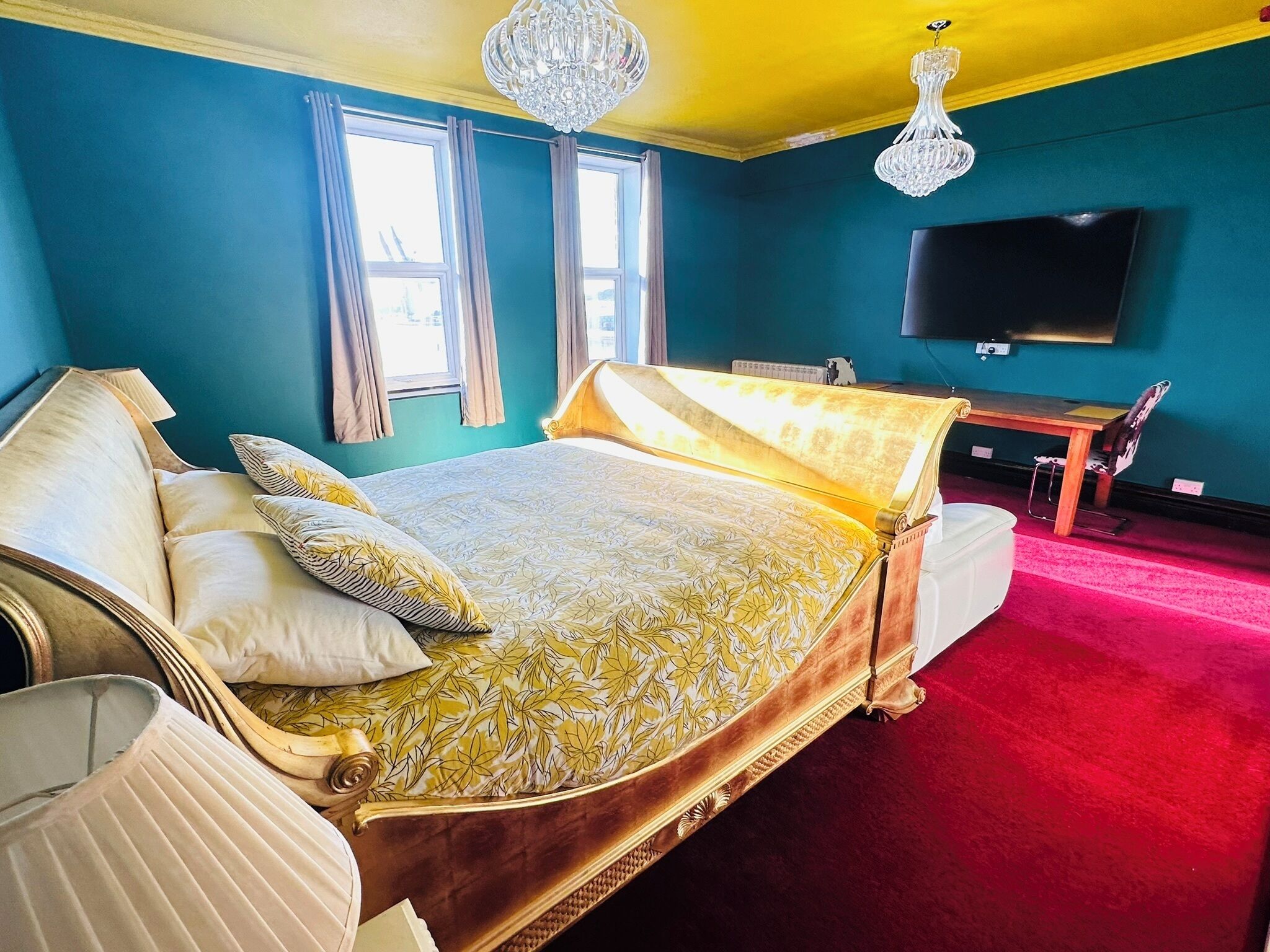 A bedroom with a large bed, a desk, a television, and a red carpet.