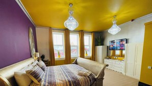 A hotel room with a large bed, a TV, a dresser, and a window with curtains. - PHOENIX Apartments (Goole)