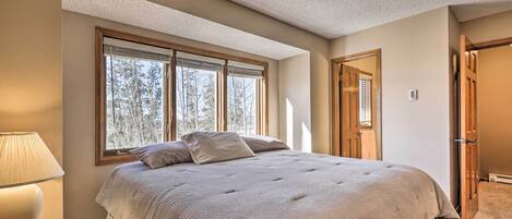A bedroom with a large bed, a nightstand with a lamp, and a window with blinds.
