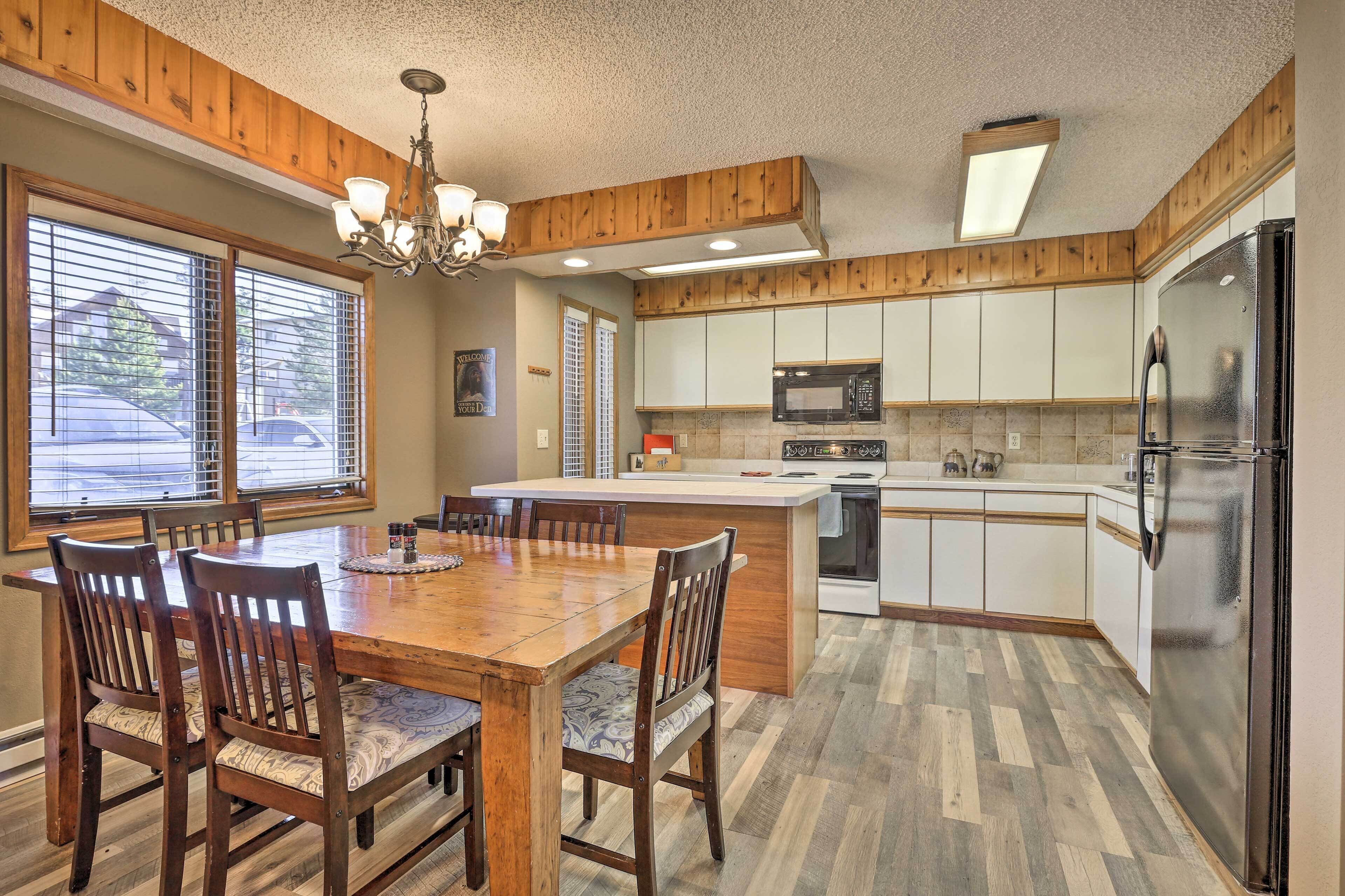 Una cocina con armarios de madera, una isla central, una mesa de comedor con sillas y un refrigerador.