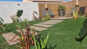 A backyard with artificial grass, a wooden deck, potted plants, and a pergola with a bamboo fence.