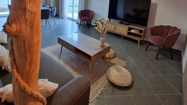 A modern living room with a large wooden tree trunk centerpiece, a flat-screen TV, comfortable seating, and a decorative hanging light fixture.