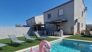 A swimming pool with a pink flamingo float, a house with a tiled roof, and outdoor seating.