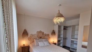 A bedroom with a large bed, two bedside tables, a wardrobe, and a hanging light fixture.