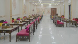 Een hotelkamer met een lange gang, houten tafels met roze kussens, en een betegelde vloer.