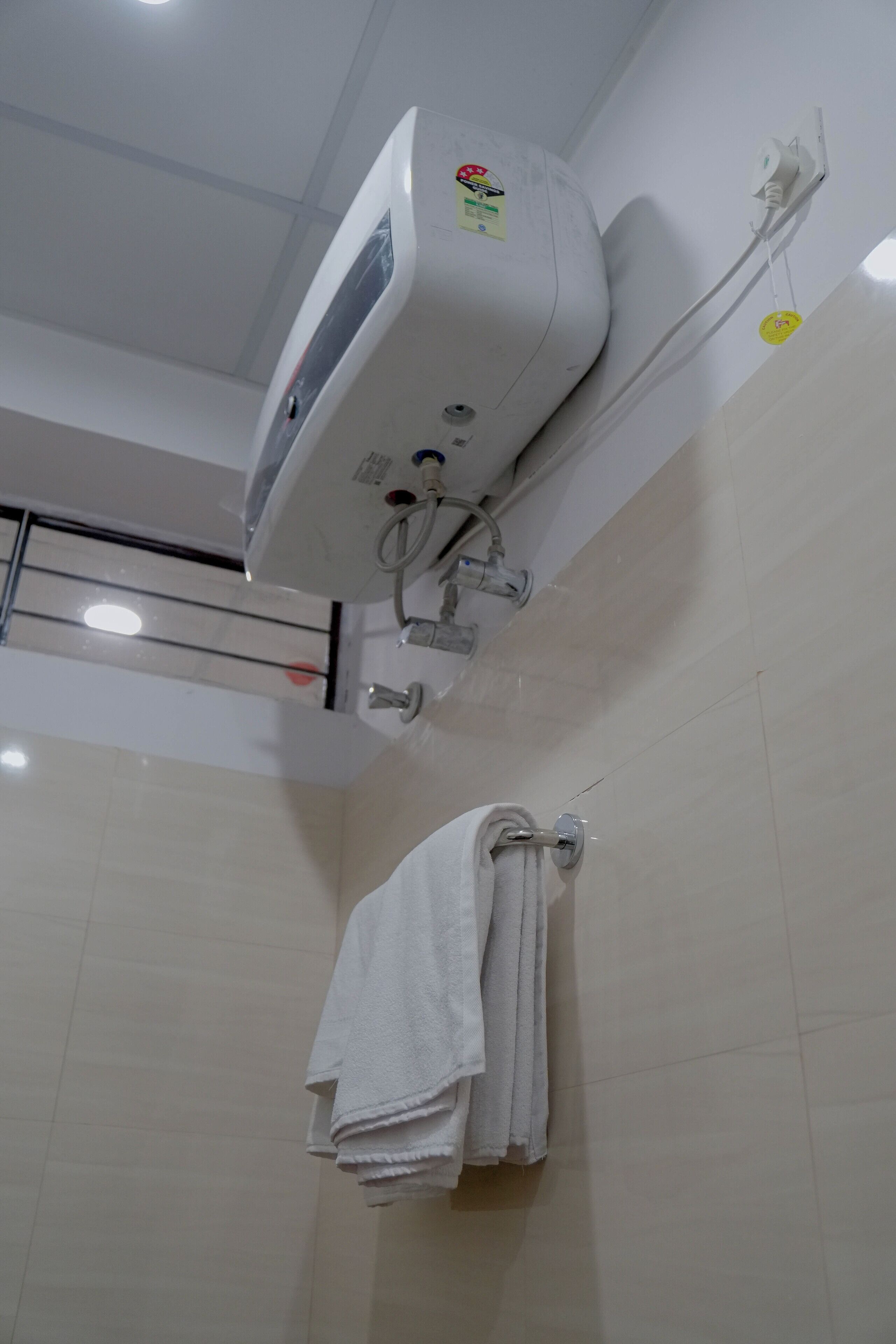A bathroom with a white air conditioning unit mounted on the wall, a towel rack with folded towels, and a visible showerhead.