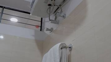 A bathroom with a white air conditioning unit mounted on the wall, a towel rack with folded towels, and a visible showerhead.