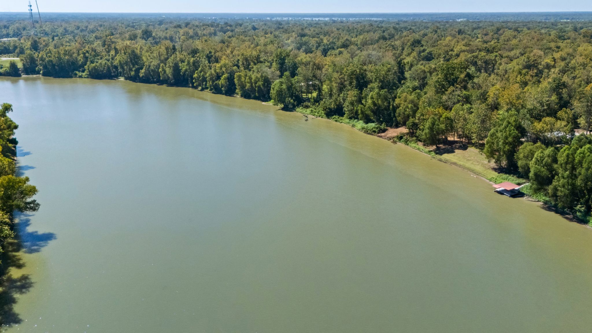 A river surrounded by dense forest with a small building near the shore.