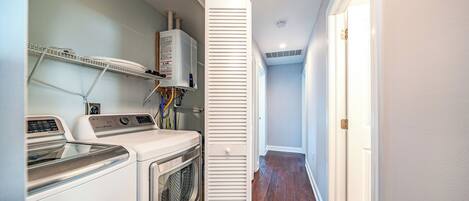 A laundry room with stacked washer and dryer units, a water heater, and a vented cabinet.