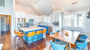 A modern kitchen with white cabinets, a central island with bar stools, and a dining table with blue chairs. - Ocean City Beach Block: 5BR/4BA with Full Linen Service- Perfect for Family! (Ocean City)