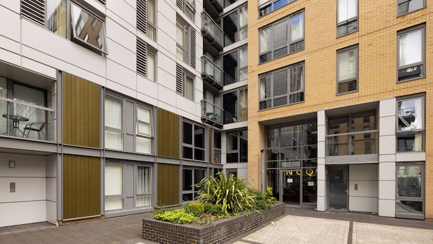 A modern building with multiple floors, large windows, and a central courtyard with plants. - Modern 1 bed flat in Greenwich (London)