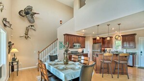 A spacious kitchen with wooden cabinets, a central island with bar stools, and a dining area with a table set for four. - Bull Shoals Retreat with Panoramic River Views – A Peaceful Escape Awaits! (Bull Shoals)