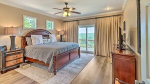 A bedroom with a large bed, a ceiling fan, a TV, and a view of the outdoors. - Bull Shoals Retreat with Panoramic River Views – A Peaceful Escape Awaits! (Bull Shoals)