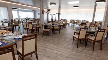 Un comedor amplio con múltiples mesas y sillas, ventanas grandes y un diseño moderno y limpio.
