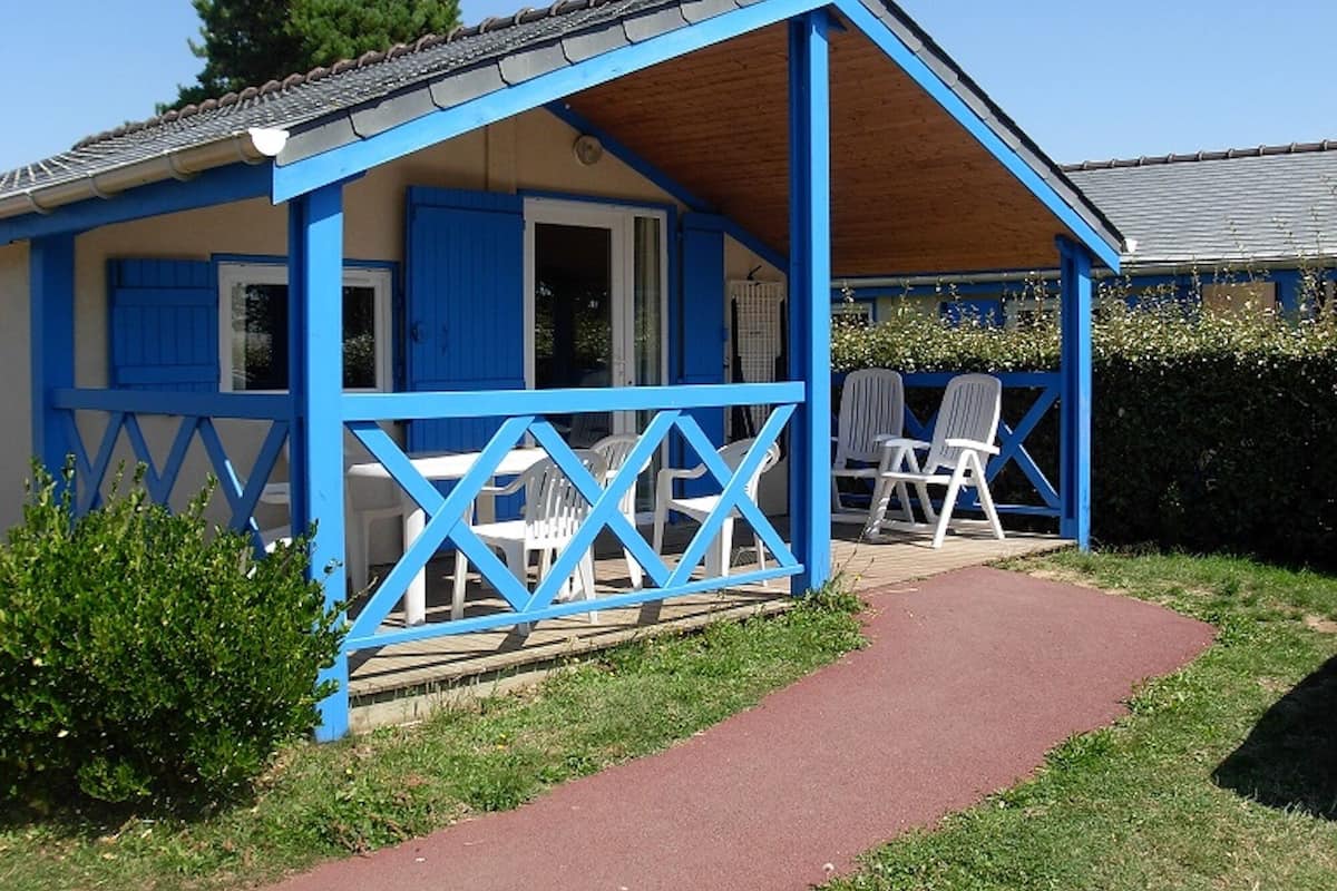 Een blauwe cottage met een overdekt terras, witte stoelen en een rode looppad.