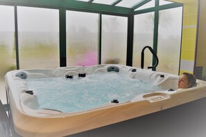 Ett bubbelbad med en person i, omgivet av en glasvägg med utsikt över palmer.