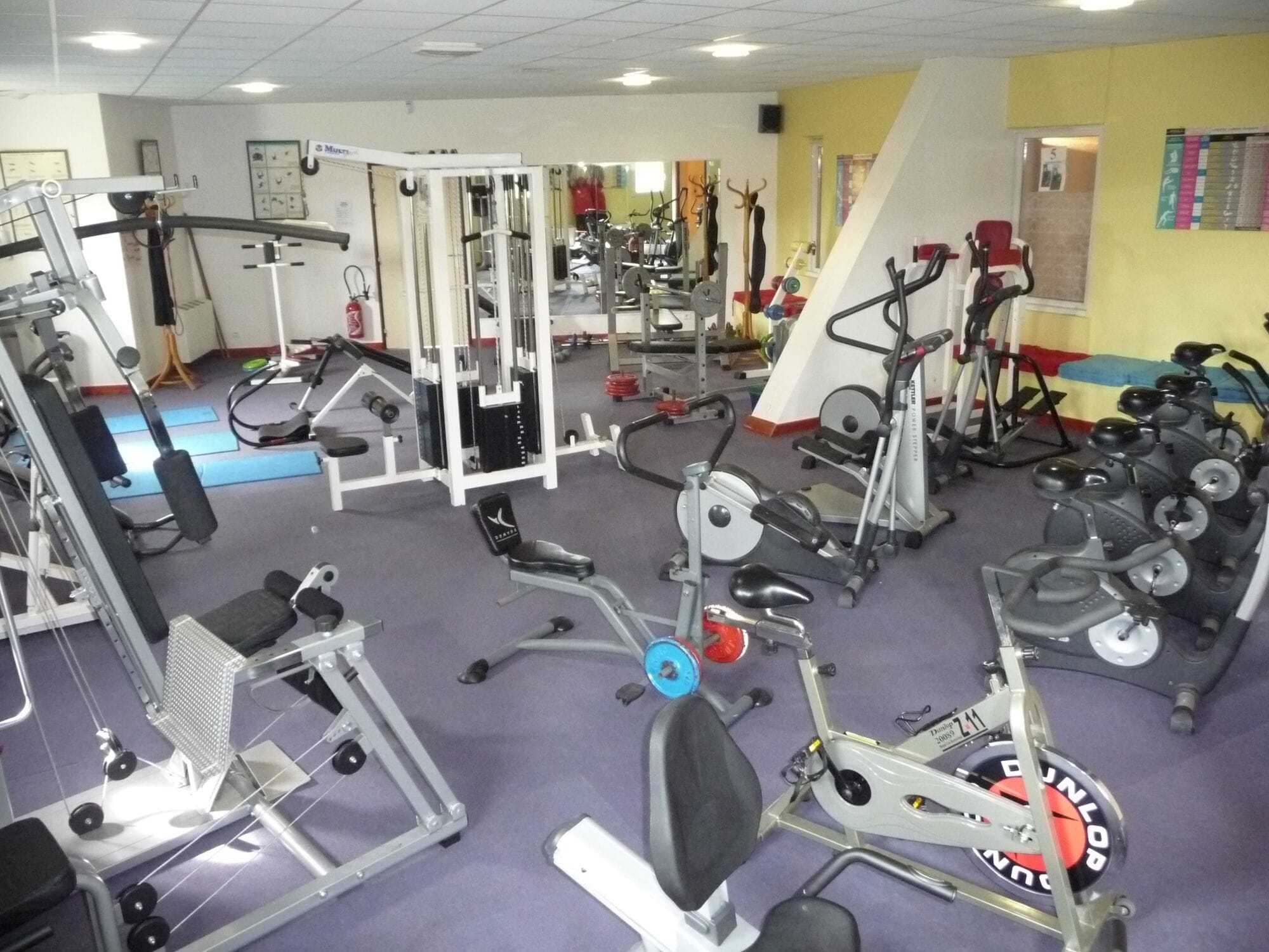 Ein Fitnessstudio mit verschiedenen Trainingsgeräten, darunter Kraftgeräte, Laufbänder und Ergometer.