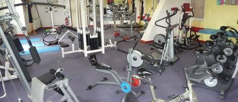 Ein Fitnessstudio mit verschiedenen Trainingsgeräten, darunter Kraftgeräte, Laufbänder und Ergometer.