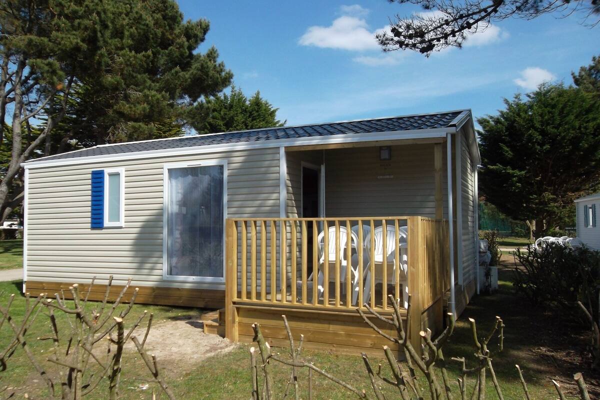 Een kleine, gelijkvloerse stacaravan met een veranda, een deur en een raam.