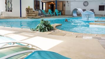 En indendørs swimmingpool med liggestole, et lille vandfald og et ur på væggen.