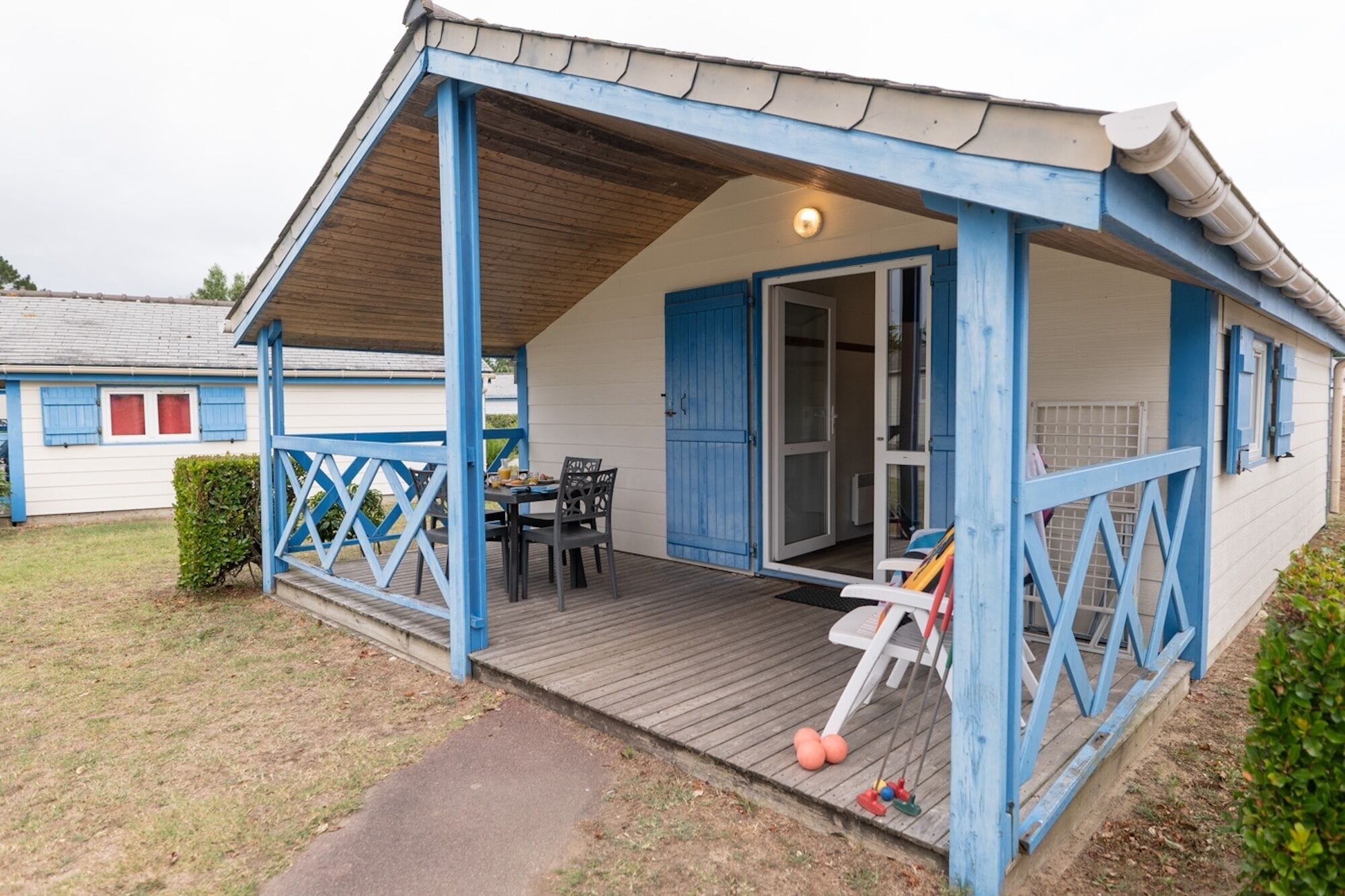 Un espace extérieur abrité, avec une table et des chaises, une porte bleue et un petit jardin.