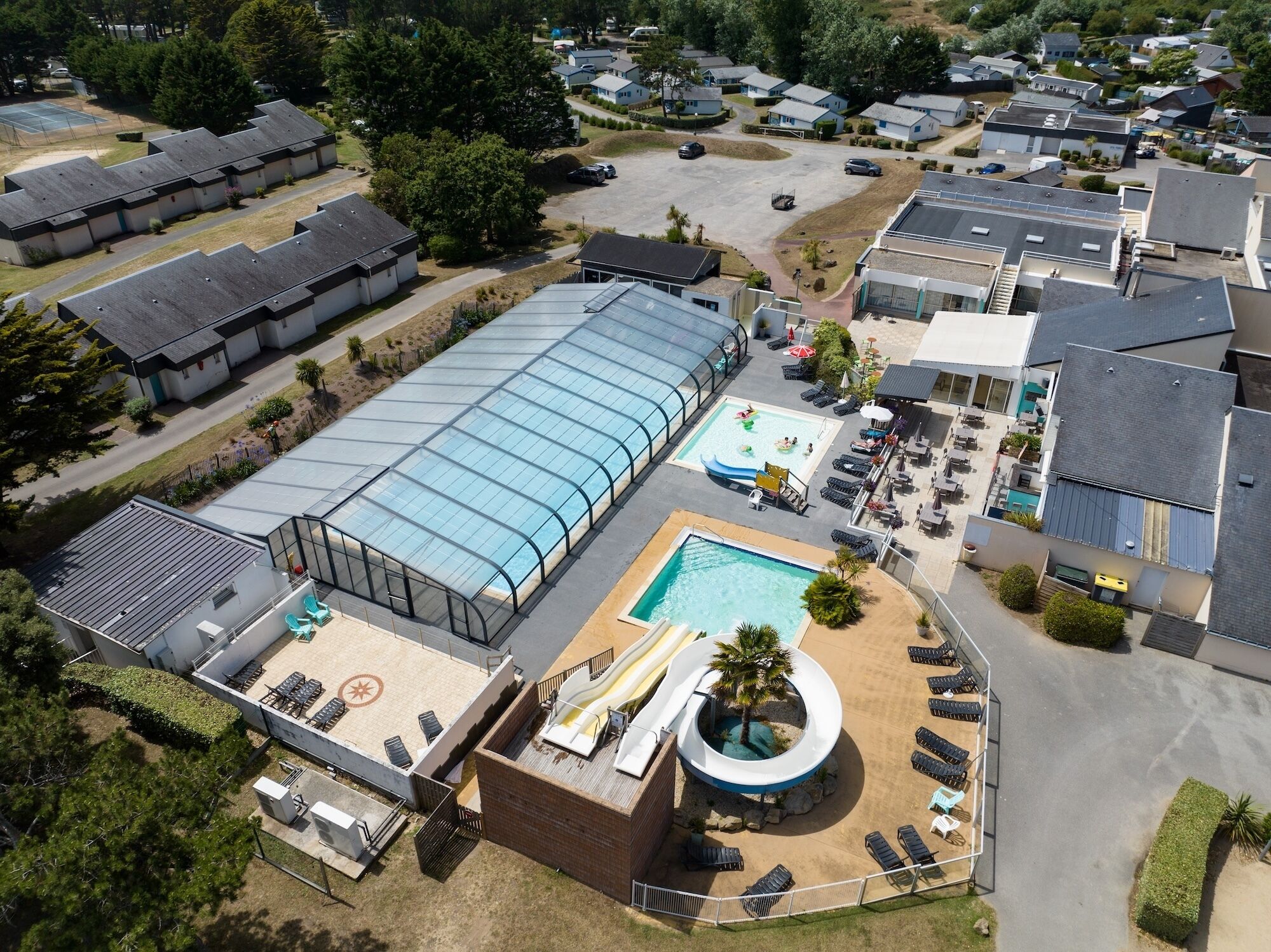 An aerial view of a resort with a large covered swimming pool, a smaller pool, and a water slide.