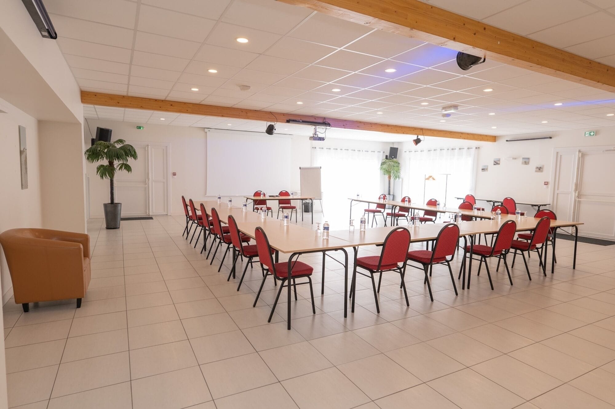 A conference room with a long table and red chairs, white walls, and a wooden ceiling.