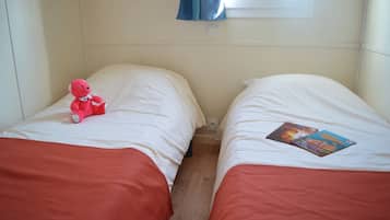 Deux lits simples avec une literie blanche et des têtes de lit rouges, un ours en peluche rose sur le lit de gauche et un livre sur le lit de droite.
