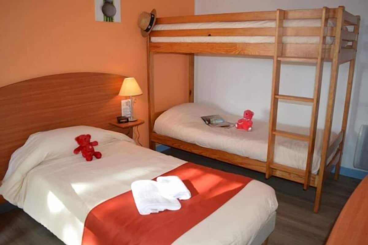 Een slaapkamer met een stapelbed, een houten hoofdeinde, een nachtkastje met een lamp en een teddybeer op het onderste bed.