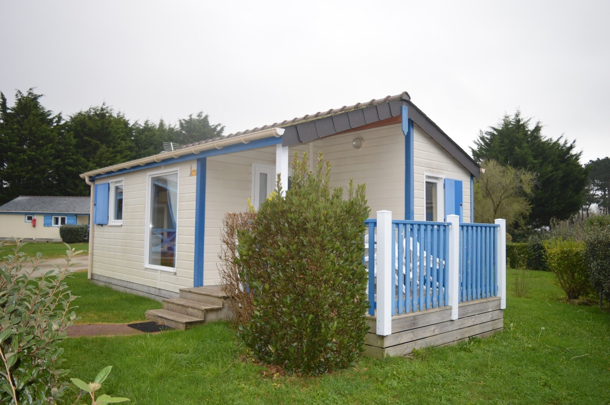 Une petite maison mobile d’un seul étage, dotée d’une véranda et d’une cour clôturée.