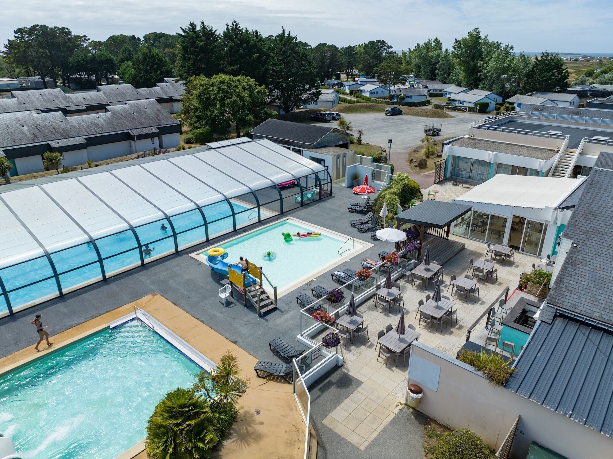 A rooftop pool area with a glass enclosure, lounge chairs, and a small play area.