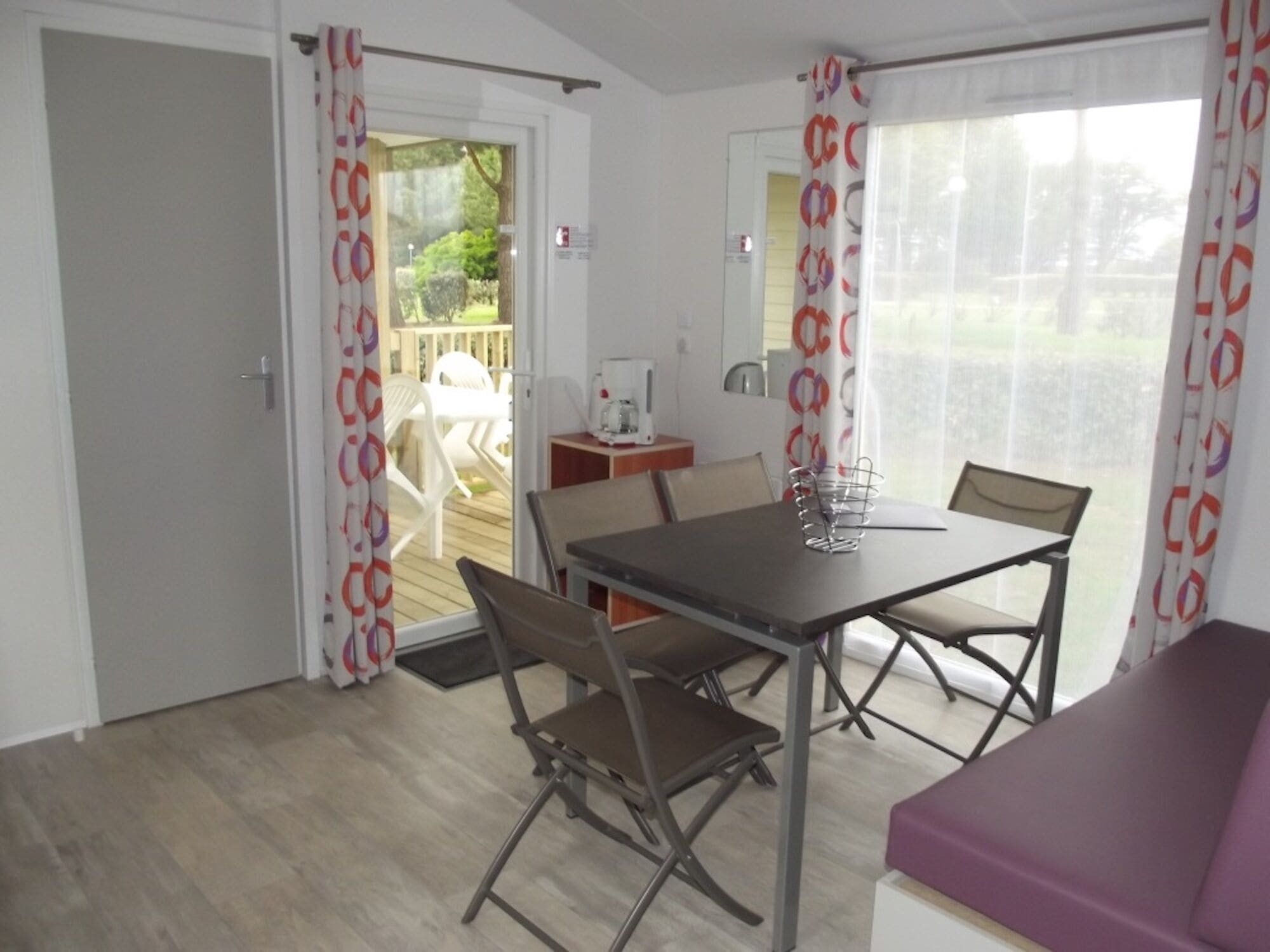 Une pièce comprenant une table et des chaises, un canapé violet et une porte donnant sur un espace extérieur avec une terrasse.