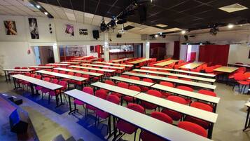 Ein Klassenzimmer mit Reihen von Schreibtischen und Stühlen, eine Bühne mit Beleuchtungstechnik und eine Tür zu einem anderen Raum.